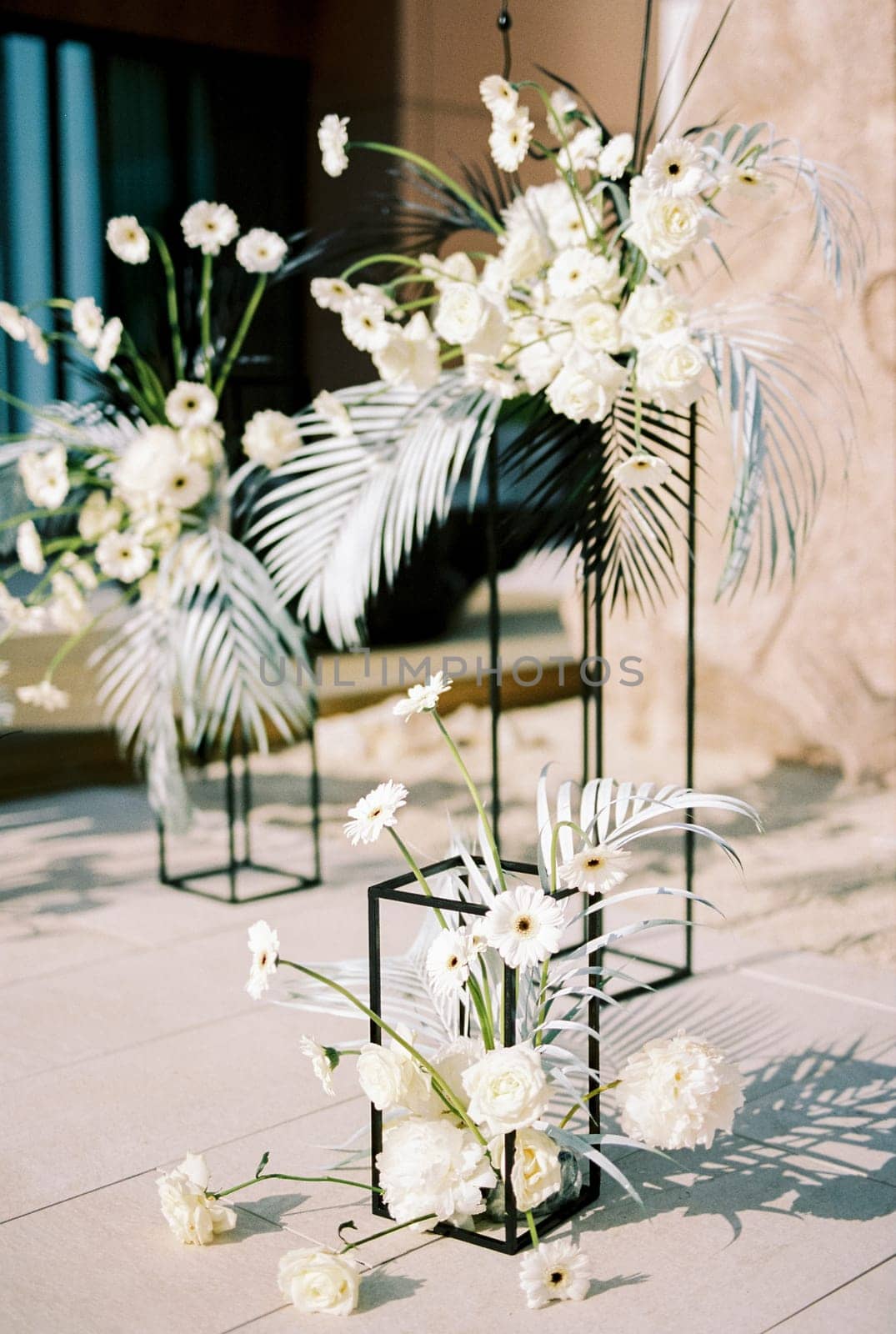 White bouquets of flowers stand on rectangular stands on tiles in the yard by Nadtochiy