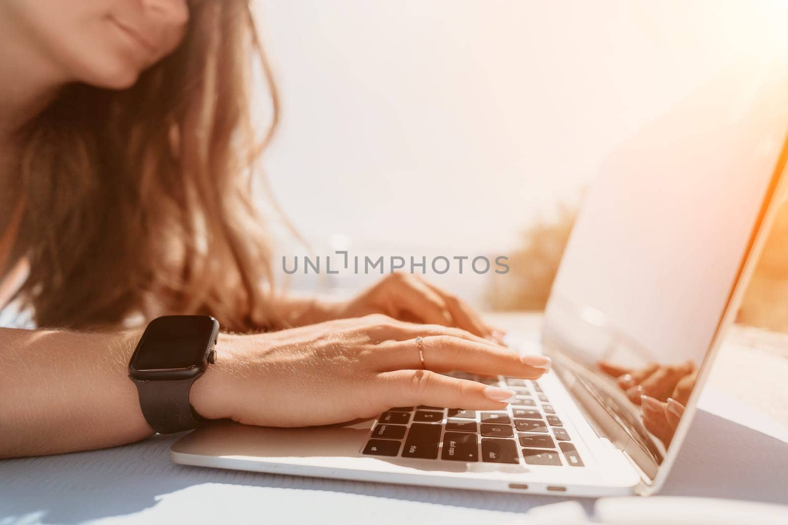 Woman laptop sea. Working remotely on seashore. Happy successful woman female freelancer working on laptop by the sea at sunset, makes a business transaction online. Freelance, remote work on vacation by panophotograph