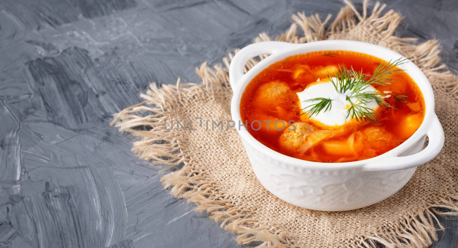 Close up borscht with sour cream in a bowl on a gray table, with copy space for text.