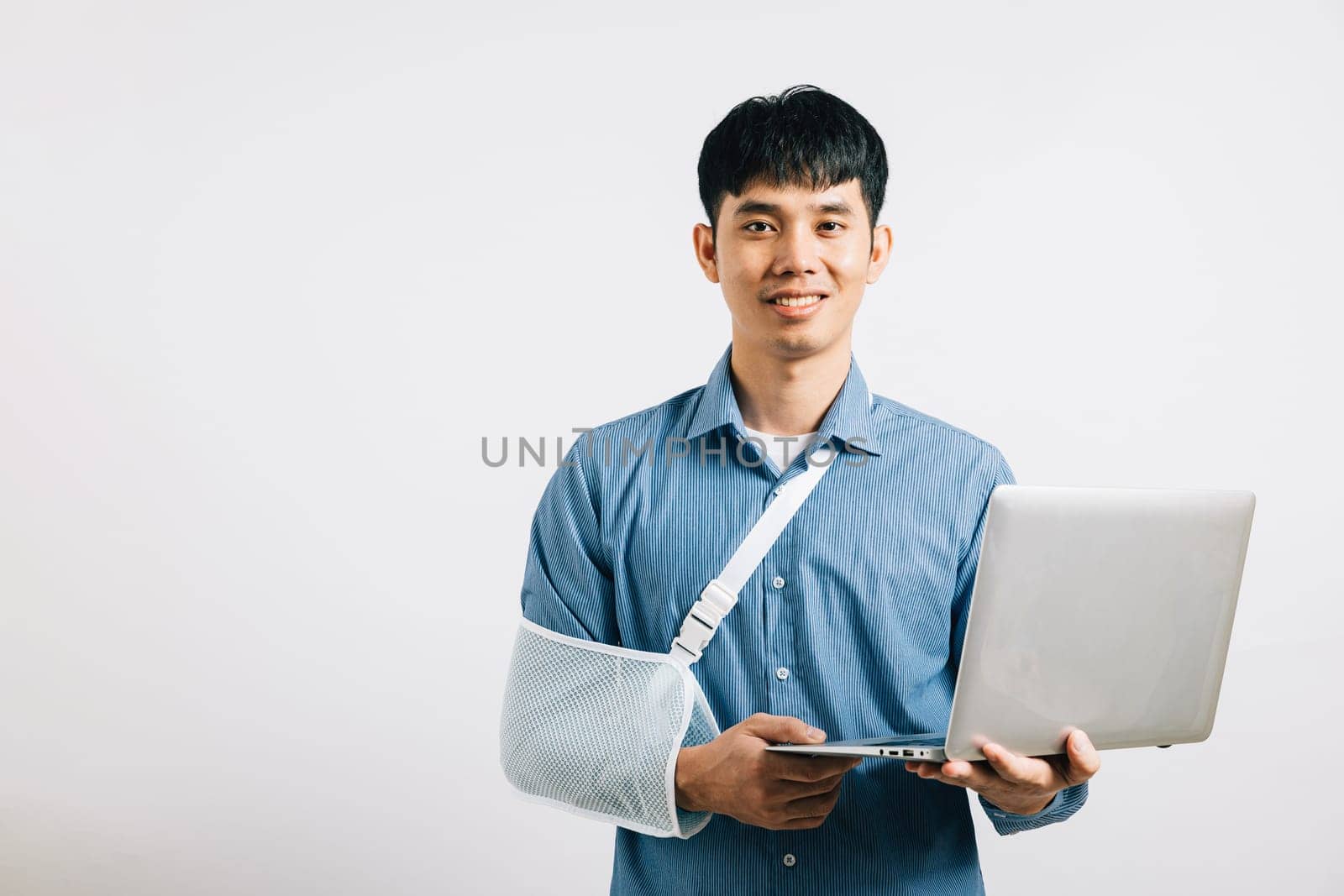 An Asian businessman, despite a broken arm, maintains confidence, using a splint for treatment while working on a laptop. Studio shot isolated on white background, emphasizing dedication and recovery.