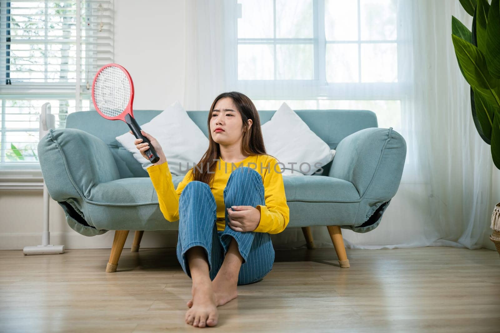 woman sitting floor using mosquito swatter or electric net racket by Sorapop