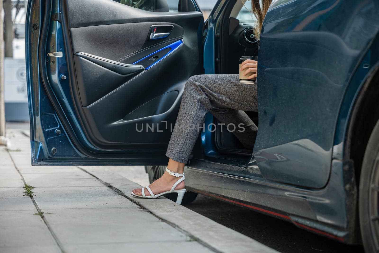 In a city setting a businesswoman in a stylish suit sits in a luxury car. Her slender leg clad in high heels gracefully opens door showcasing the blend of modern transportation and corporate glamour. by Sorapop