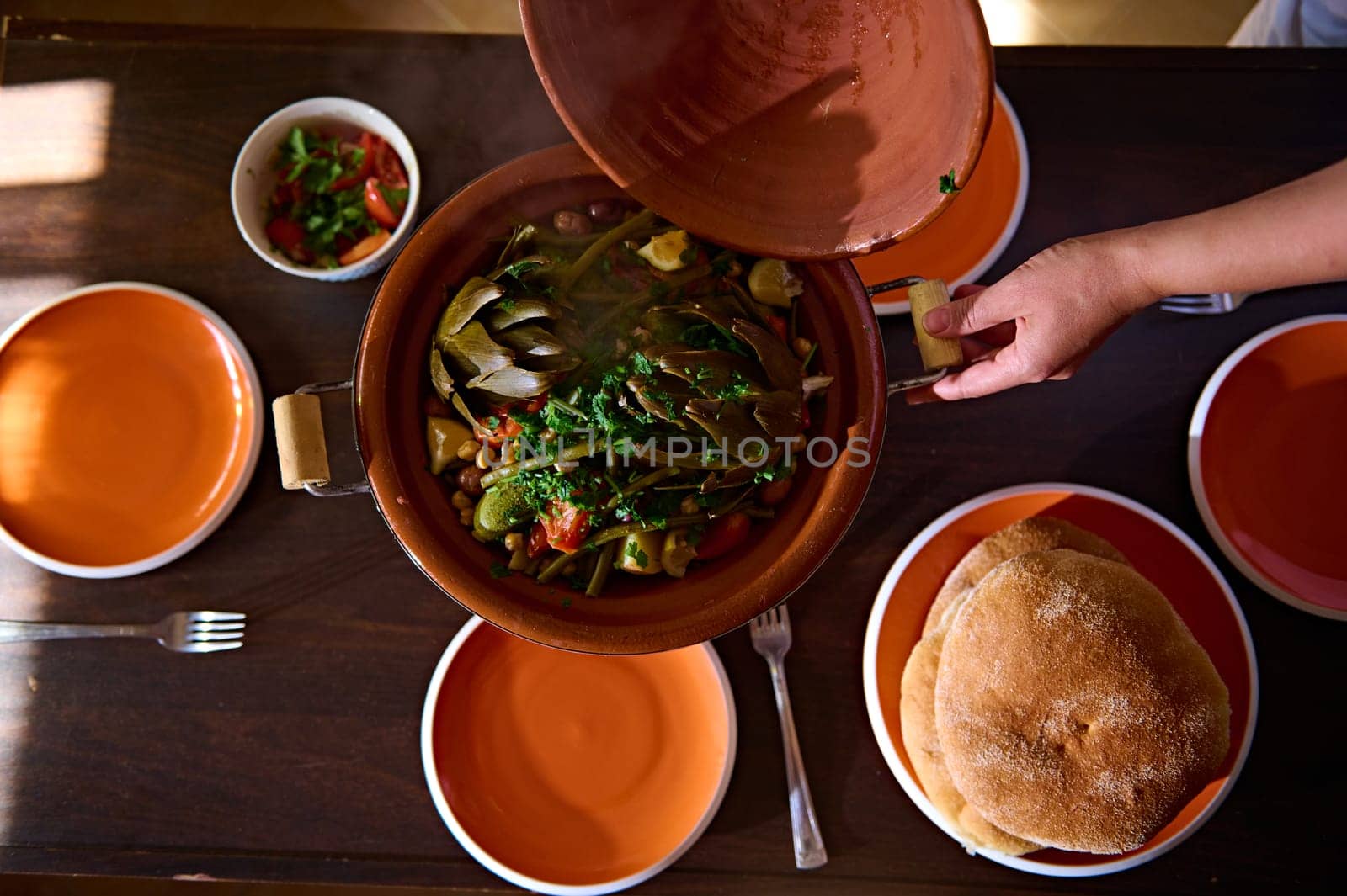 Food background with Moroccan tagine cooked at home. View from above of organic healthy vegetables, artichoke, beans, tomatoes teamed in a clay pot, cooked according to traditional Moroccan recipe