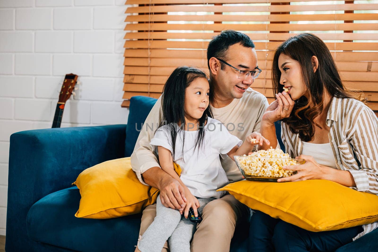 Family bonding with popcorn watching a movie in the living room by Sorapop