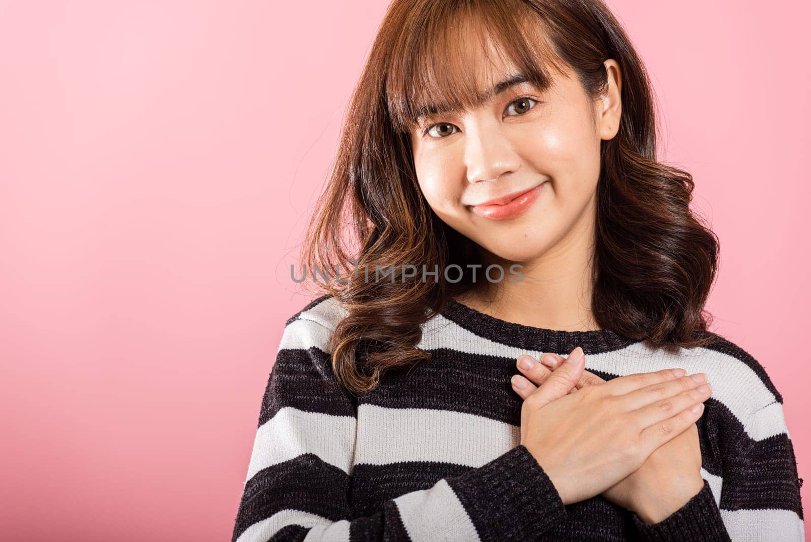 Portrait of a woman in casual attire meditating with hands close to her chest and a grateful smile by Sorapop