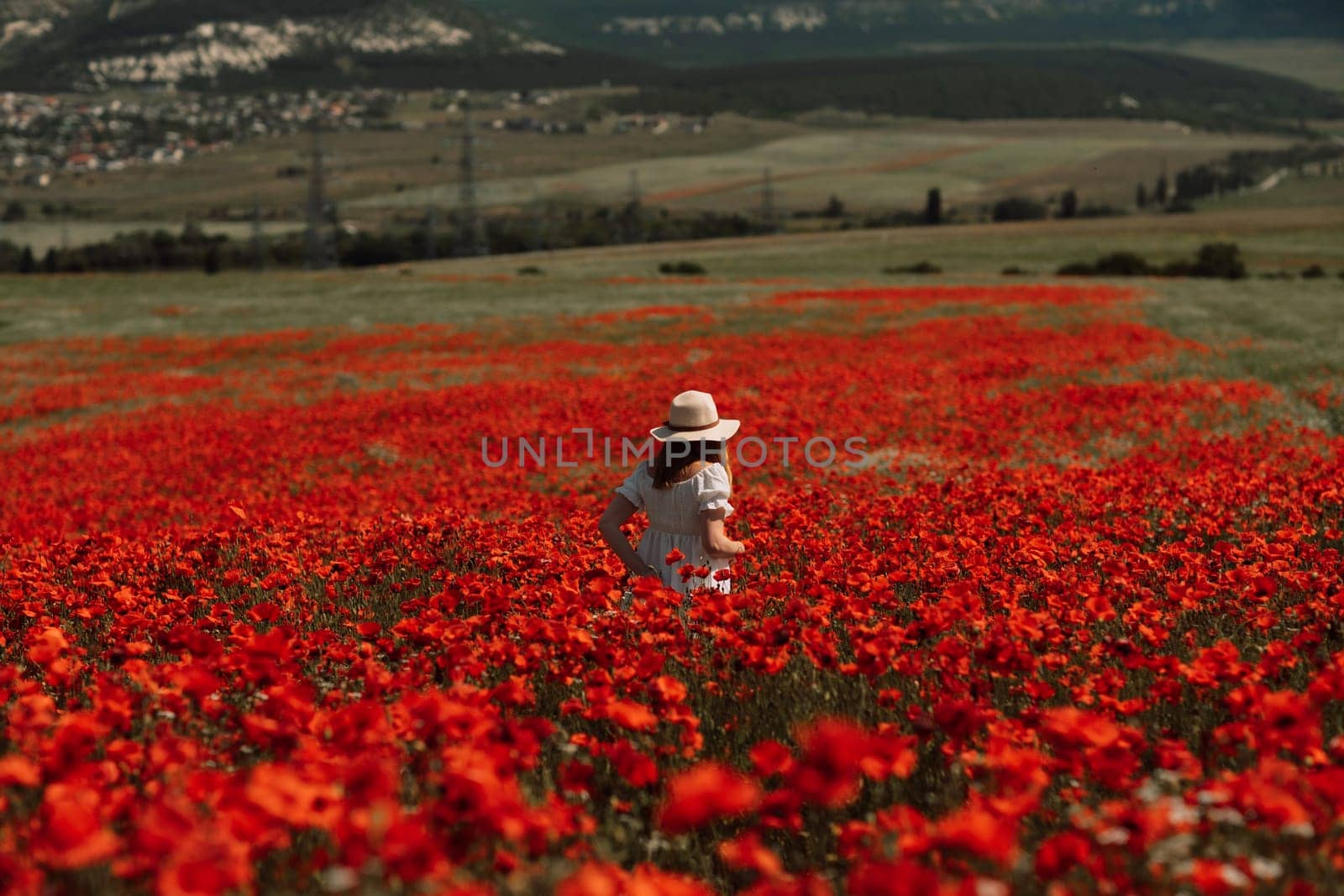 Field poppies woman. Happy woman in a white dress and hat stand with her back a blooming field of poppy. Field of blooming poppies. by Matiunina