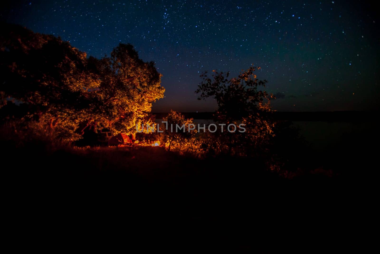 Tourists enjoying the night sky on the lake with a tent by the fire