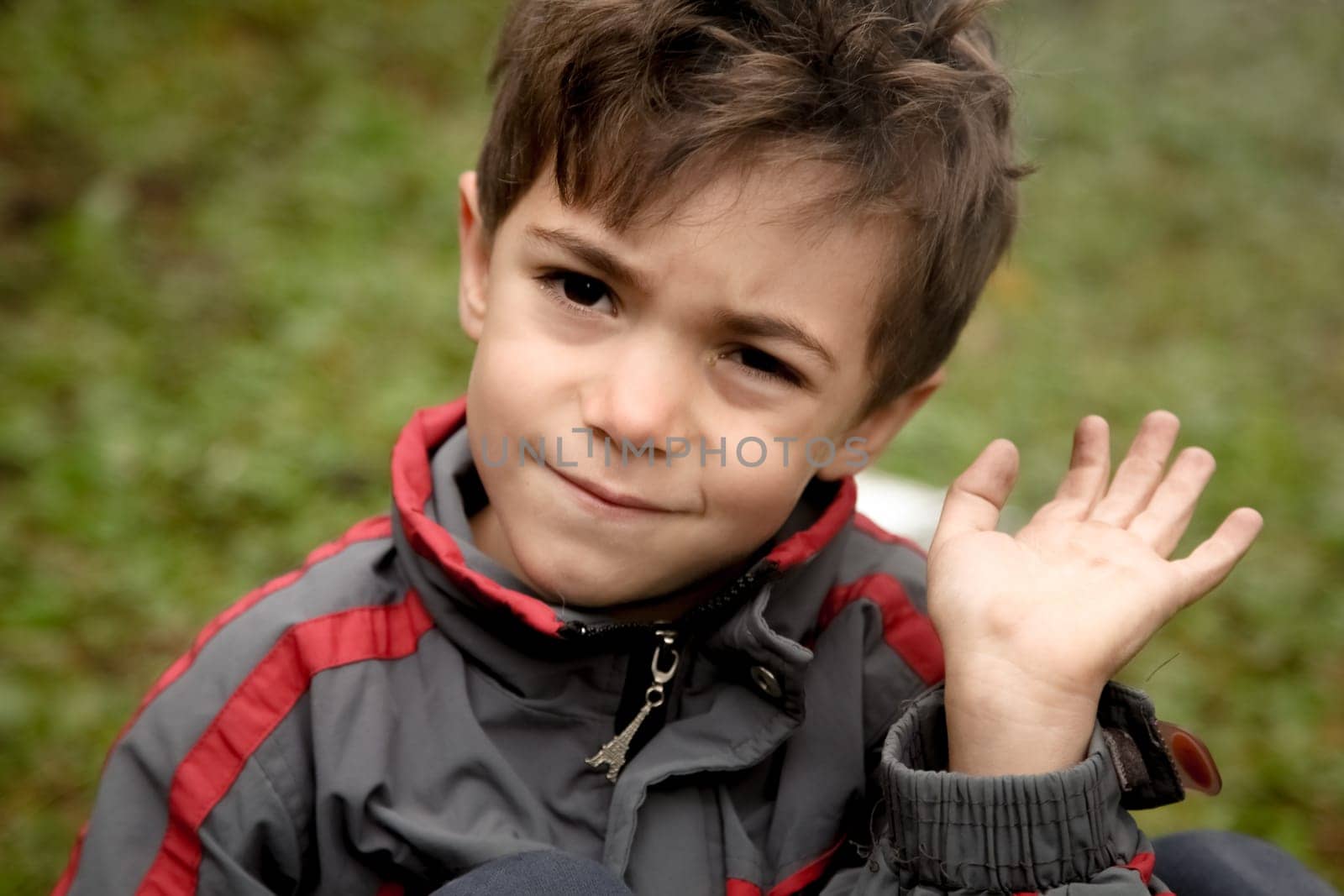 A crying arab child waving his hand. A boy wearing gray sport suit with red ribbons and eiffel tower on the clasp