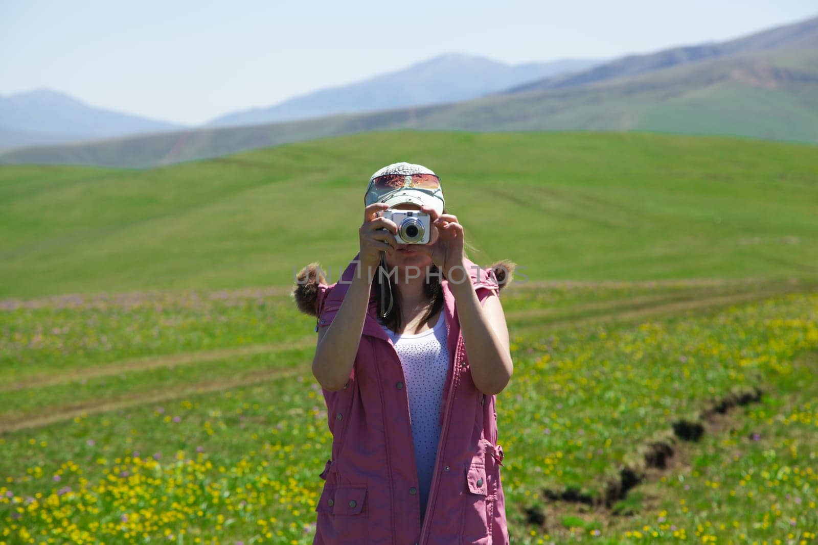 A woman in a pink waistcoat and a turquoise baseball cap photographs mountains