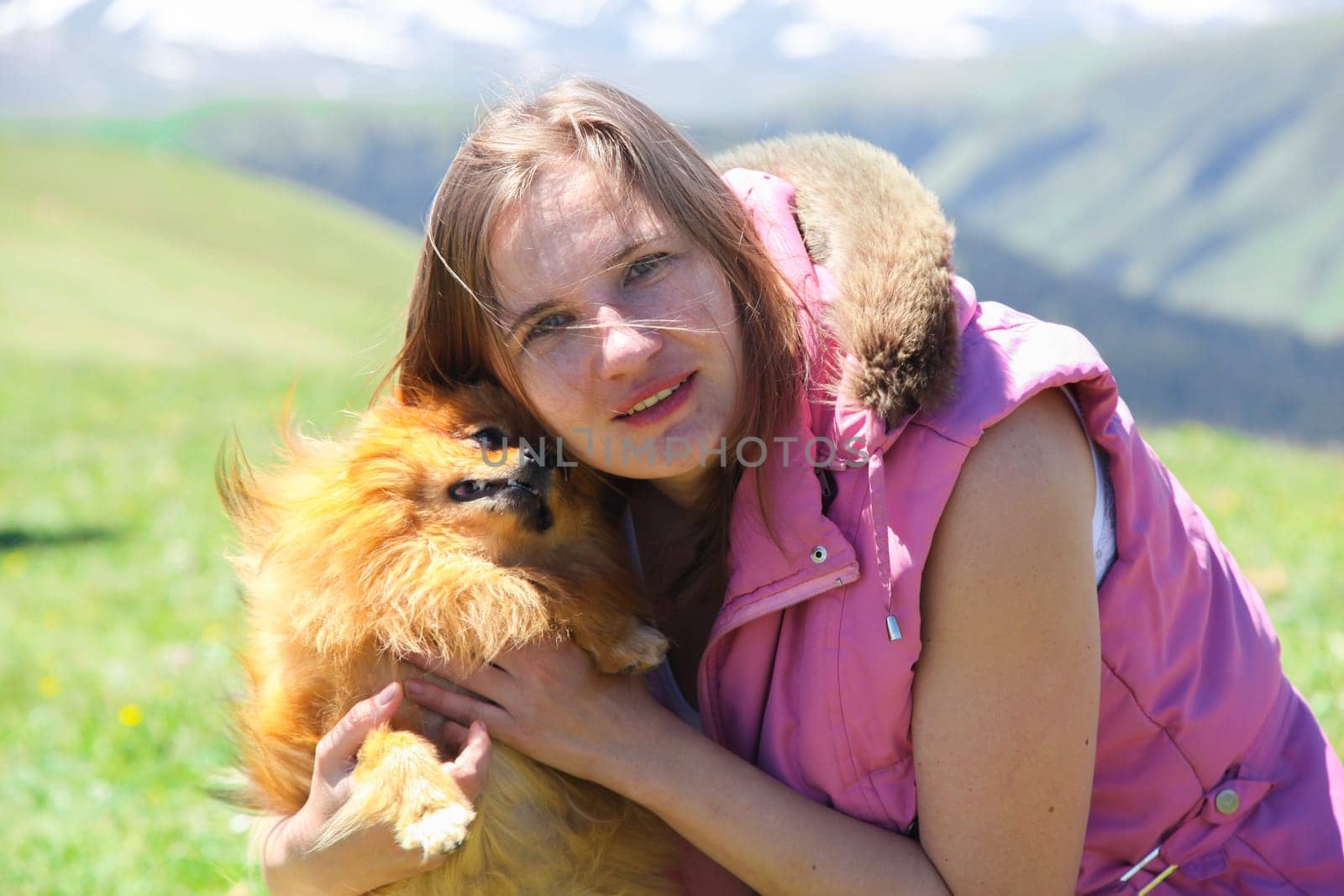 A small red dog (Pomeranian Spitz) licks a woman's face forcing her to laugh