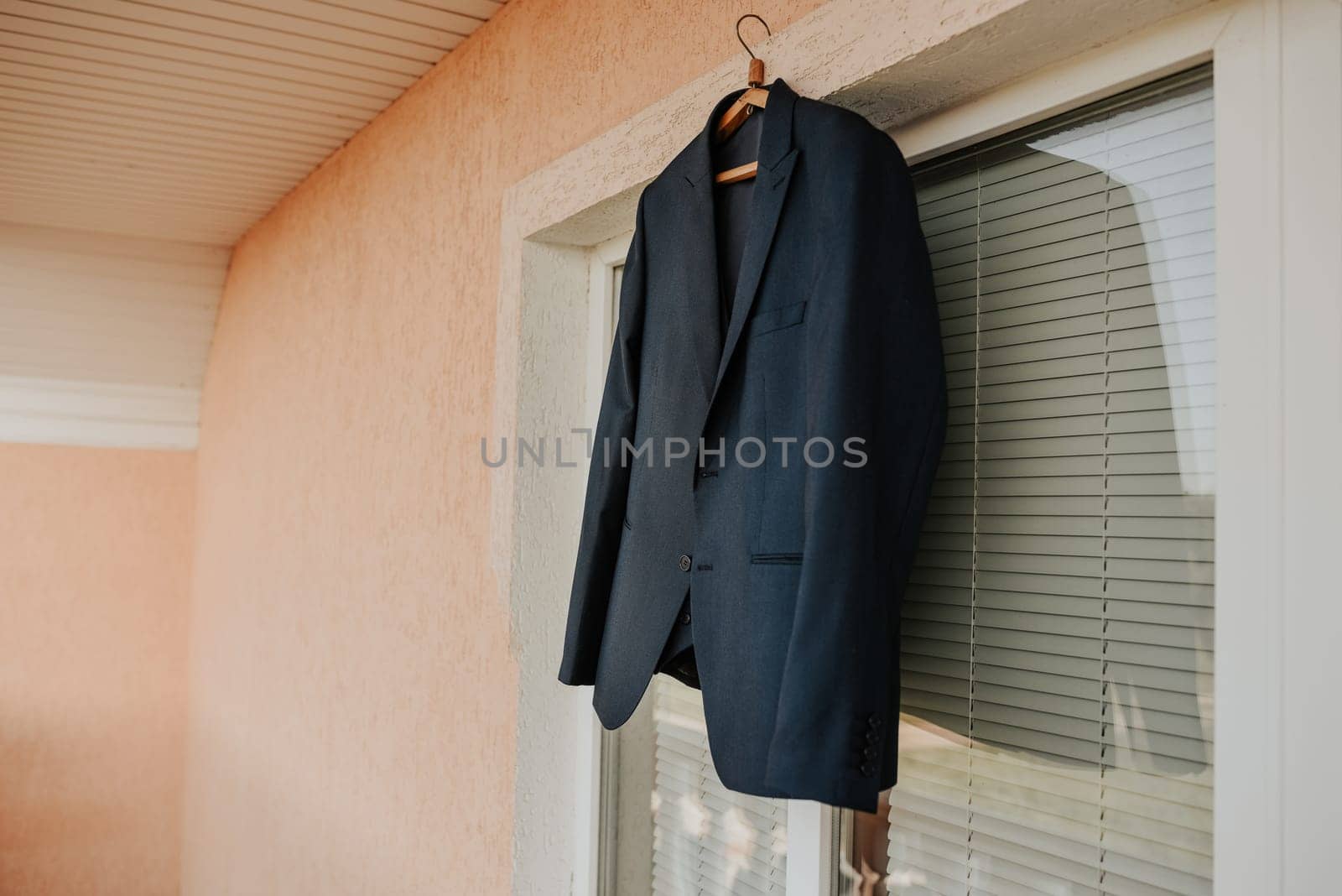 A black jacket hangs against a white window in the room. by AndriiDrachuk