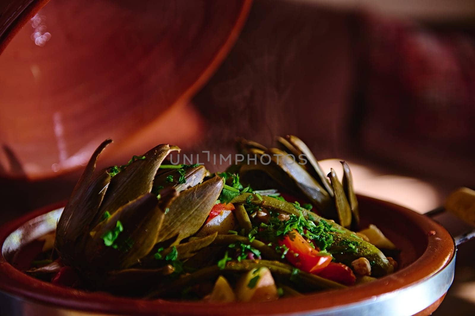 Close-up view vegetarian meal of artichoke and veggies steamed in clay dish and seasoned with fresh chopped parsley and cilantro. Moroccan tagine. Food background. Culture Cuisine Culinary Tradition