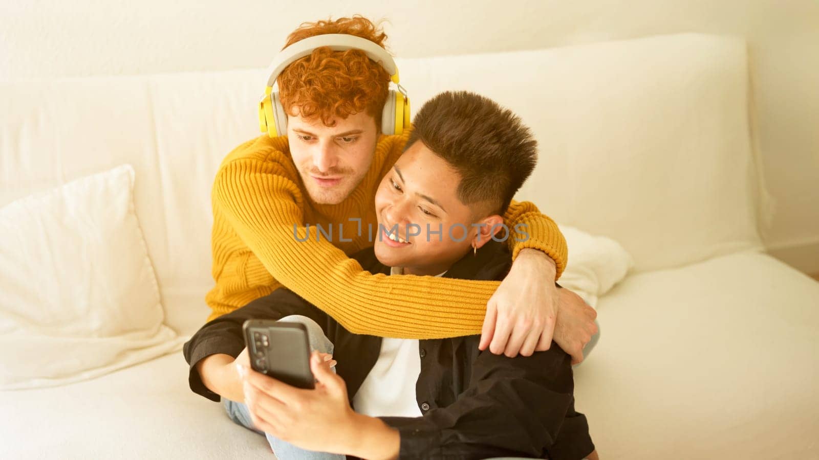 Man playing song on mobile phone for gay partner to listen to on sofa at home