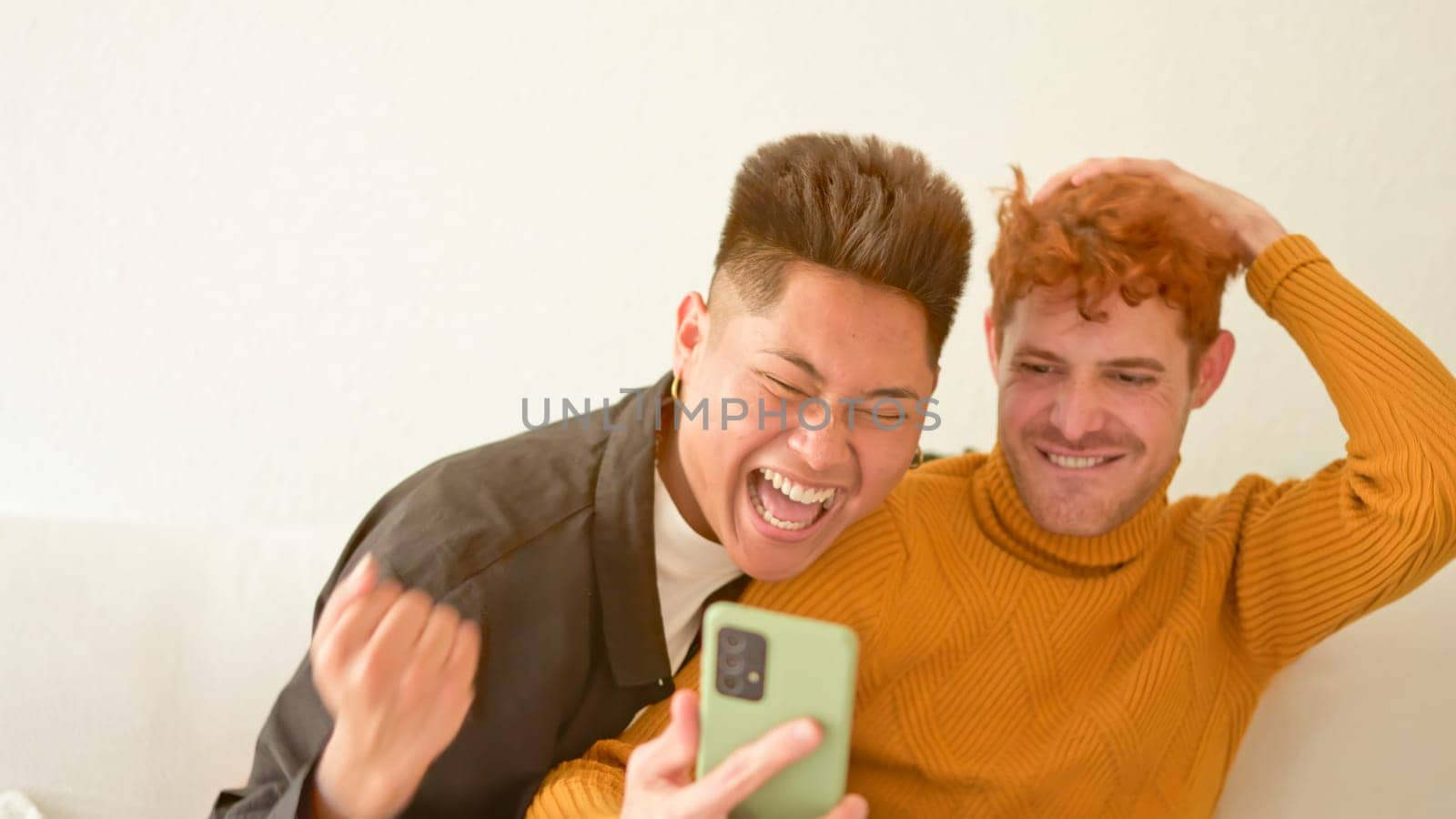 Gay couple sitting on the sofa looking at mobile phone and celebrating something