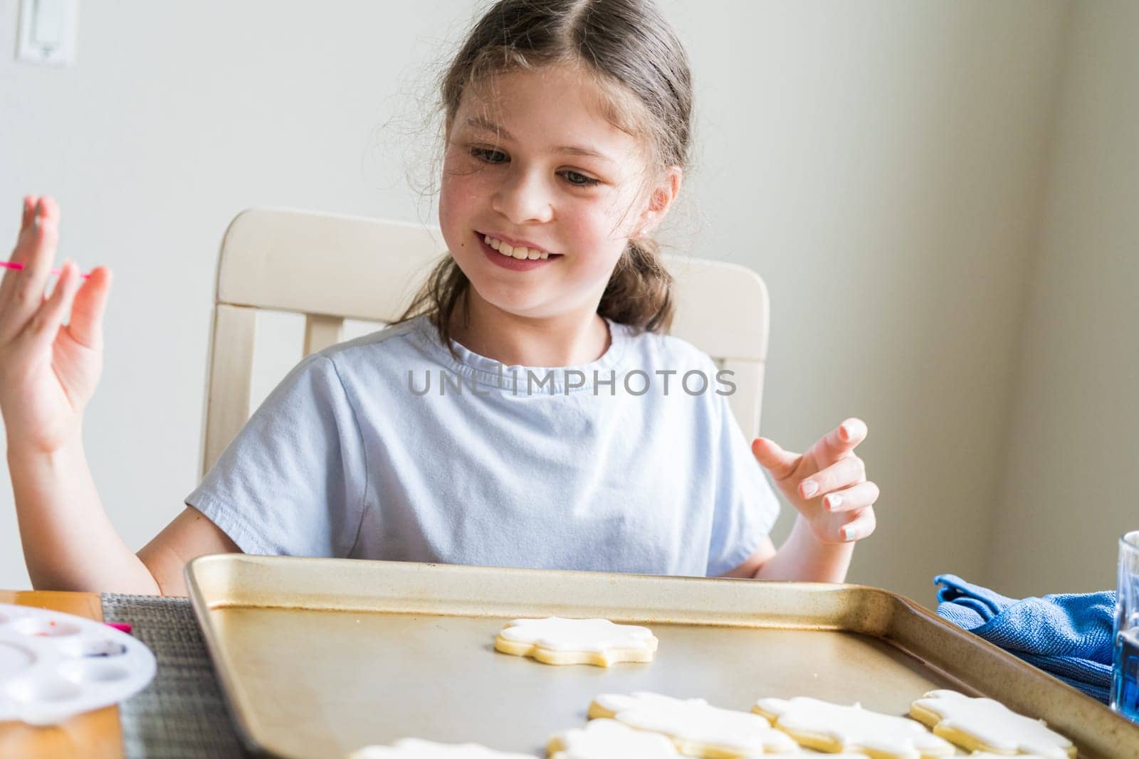 A heartwarming scene of a little girl carefully writing 'Sorry' on sugar cookies with food coloring, the cookies beautifully flooded with white royal icing.