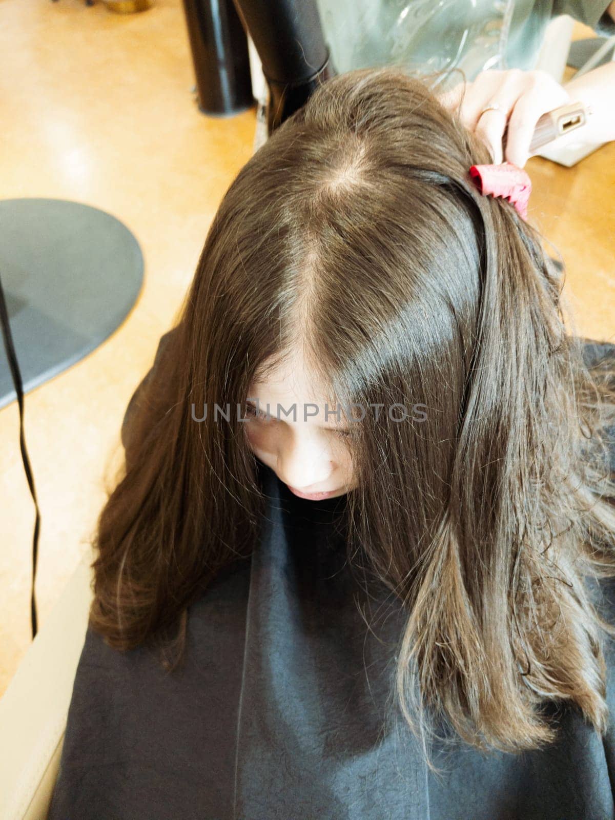 Gentle hands maneuver a hair dryer through a young girl's newly cut hair, showcasing the drying process after a meticulous trim. The warmth of the dryer breathes life into her locks, as they transform from damp to styled with care and expertise.
