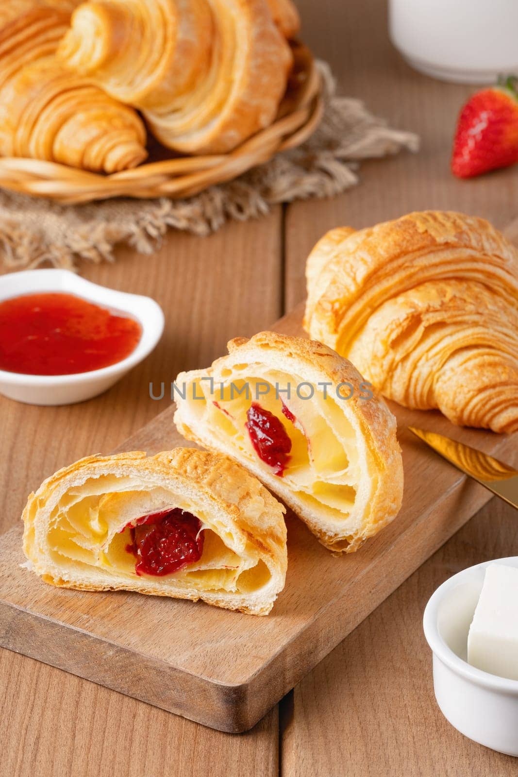 Freshly baked croissants with butter, strawberry jam and tea for breakfast.