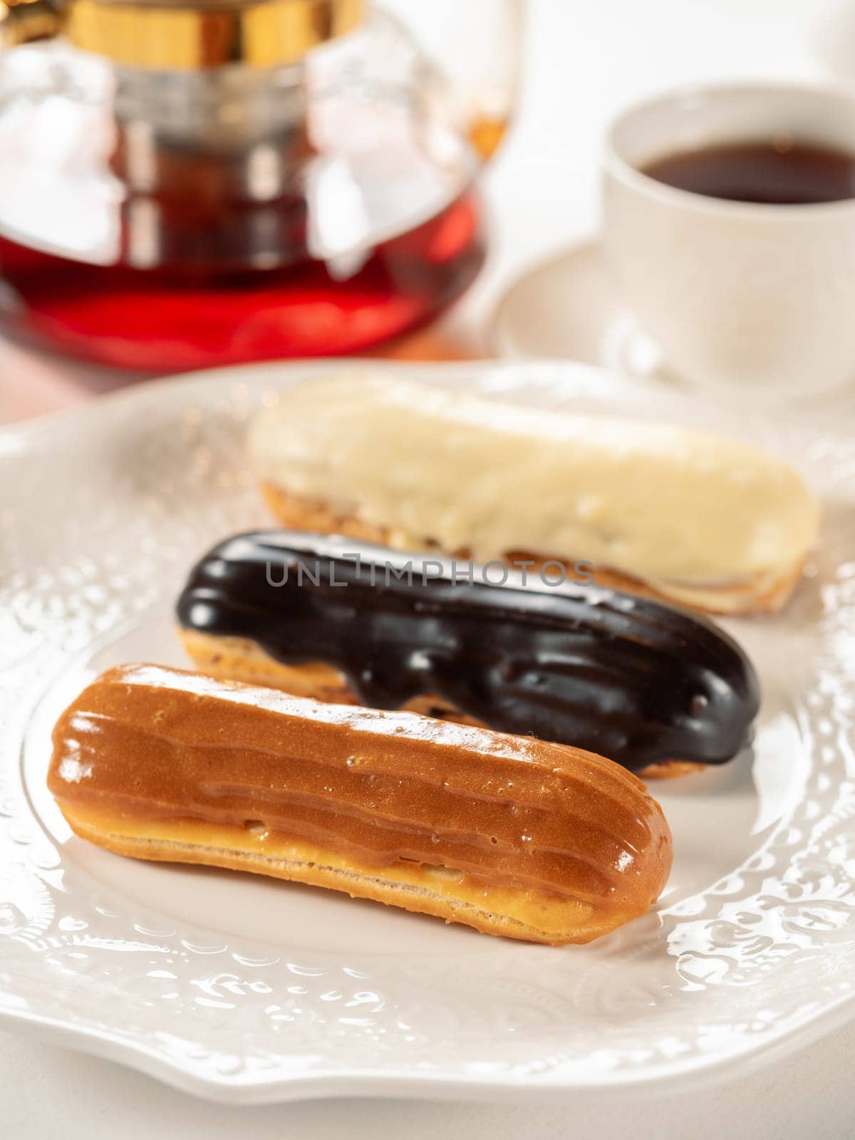 Group of french dessert Eclair on white plate. Caramel, chocolate and vanilla glazed eclairs on white plate in restaurant table background. Perfect french eclairs set