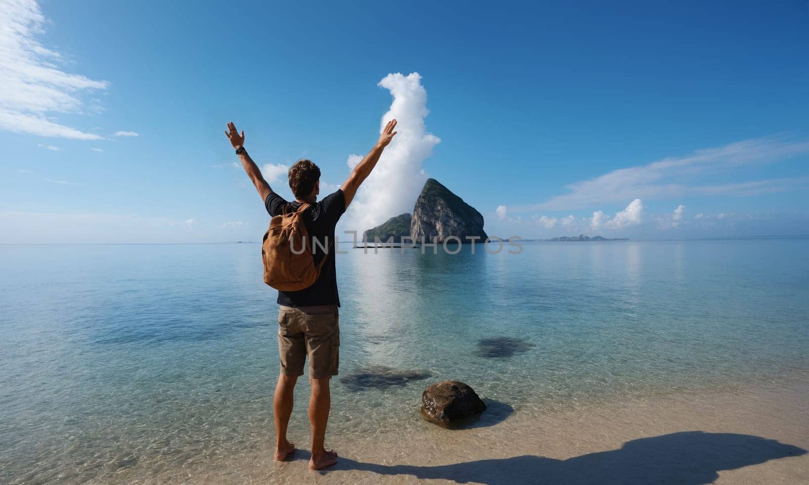 A person stands with arms raised on a serene beach. The silhouette is highlighted against the backdrop of a tranquil ocean and towering mountains.