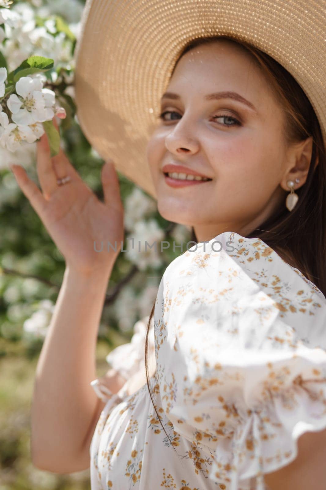 An attractive long-haired woman walks in the spring in the park of blooming apple trees. Spring portrait of a woman