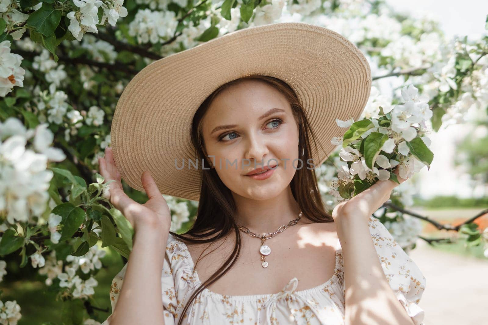 An attractive long-haired woman walks in the spring in the park of blooming apple trees. Spring portrait of a woman