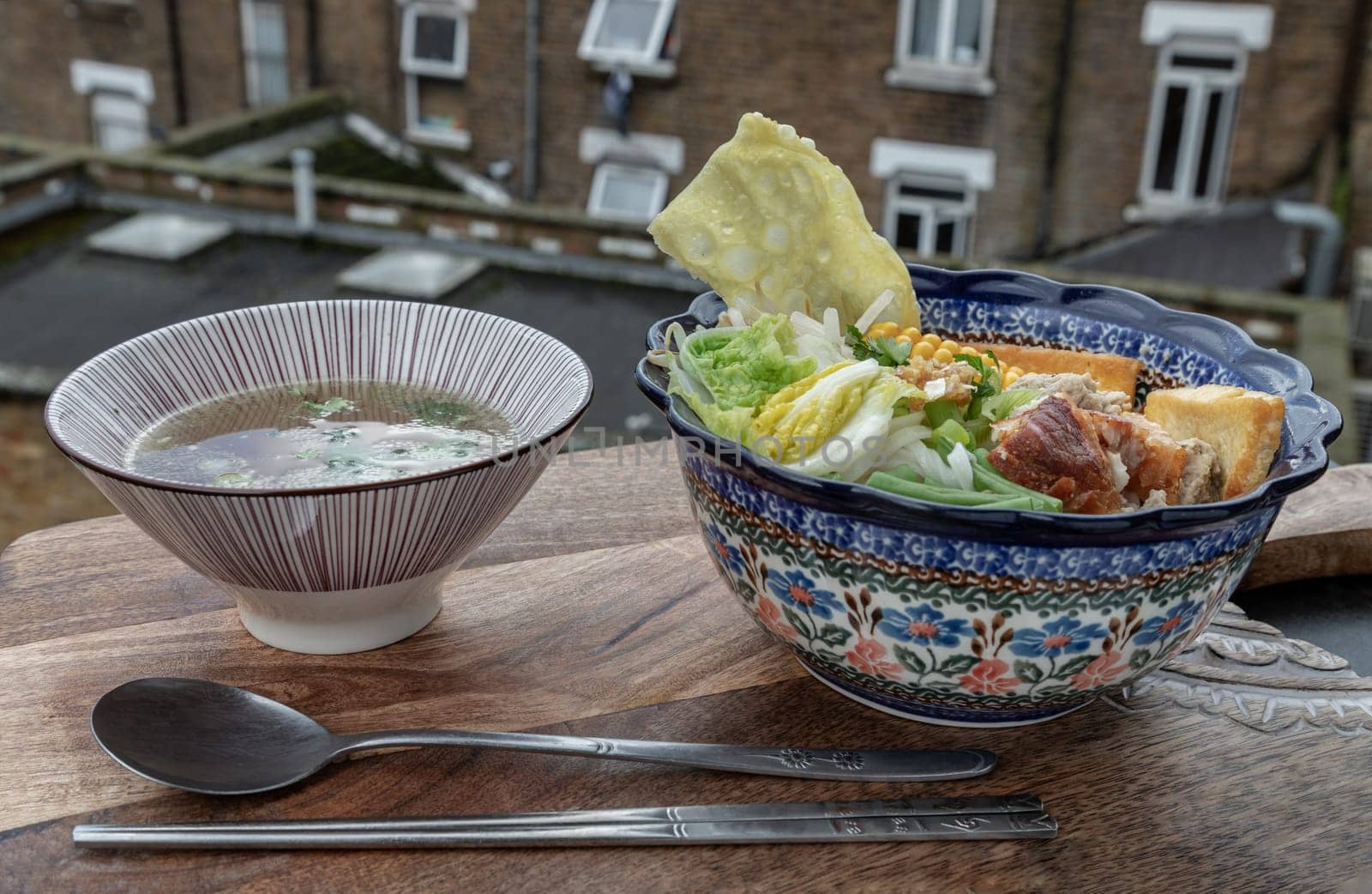 Rice stick noodles topped with Minced pork, Crispy pork, Fried wontons, Sweet corn, Fried tofu, Chinese cabbage, Yard long beans, Bean sprout, Goji berry and Coriander in Ceramic bowl served with Clear soup with spoon and chopsticks. Copy space, Selective focus.