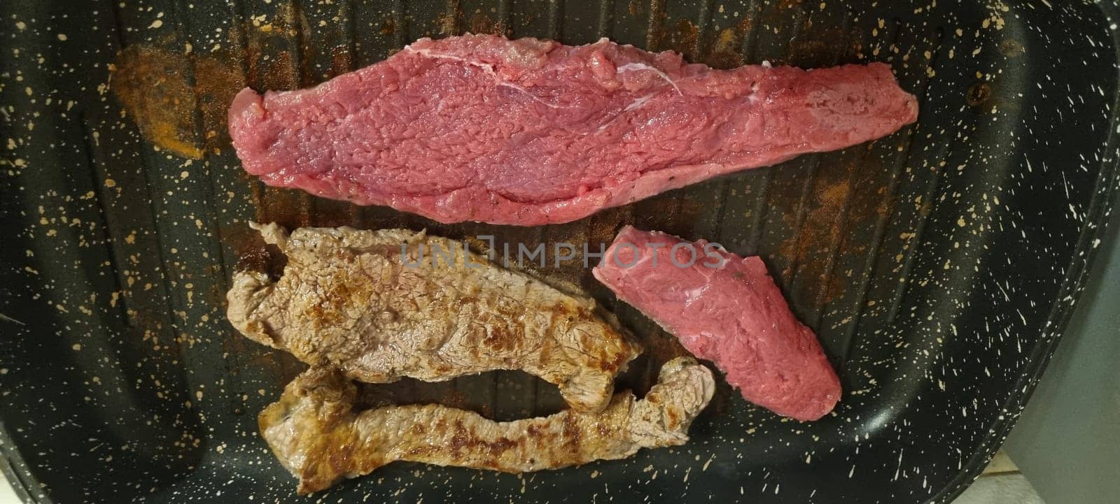 Variety of steaks in different cooking stages on a kitchen pan. Vertical image