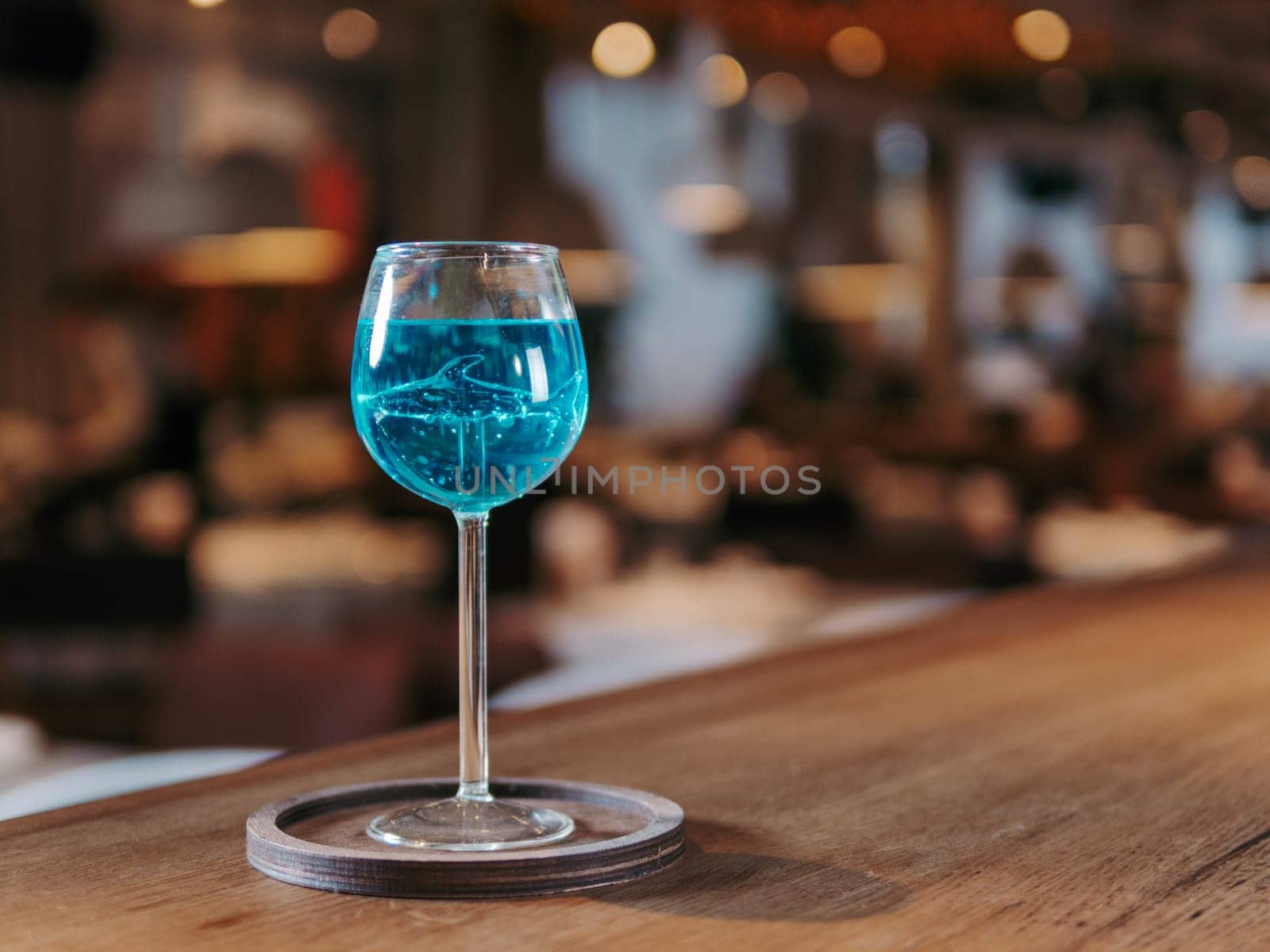 Glass of blue lagoon cocktail in shark high stem cocktail glass on beautiful bar counter background with copyspace. Aesthetic photo of blue lagoon cocktail in evening light, restaurant or bar interior