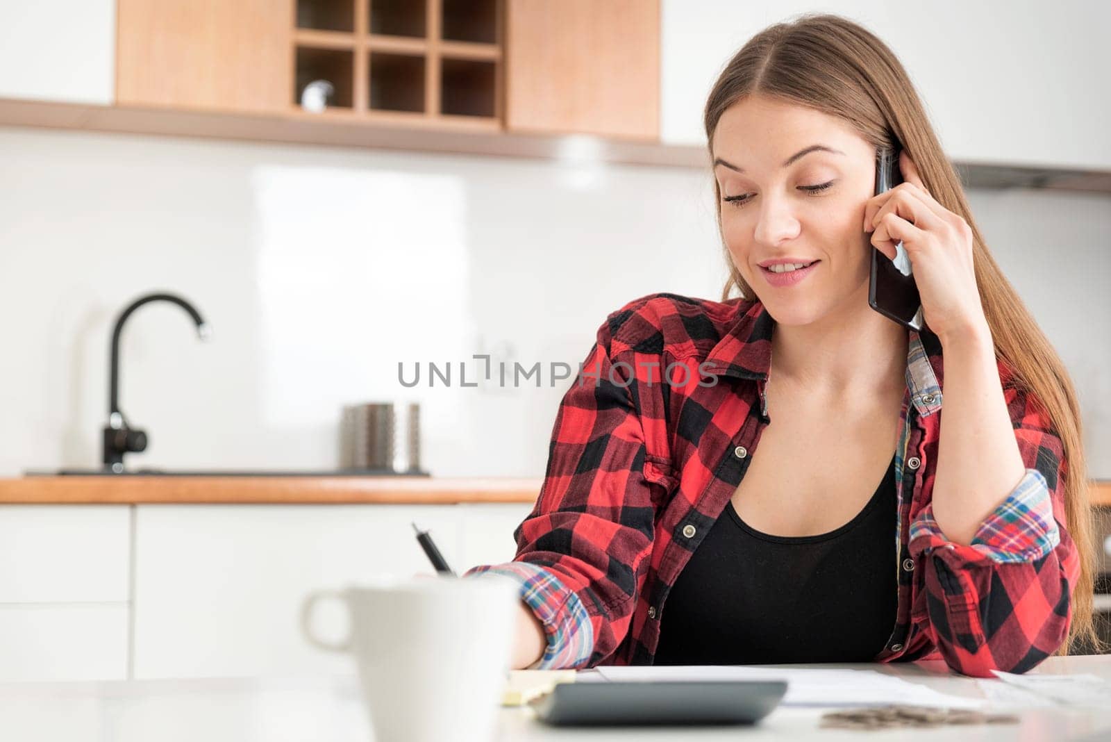 Beautiful woman talking on the phone in the kitchen. Lifestyle image with copy space.