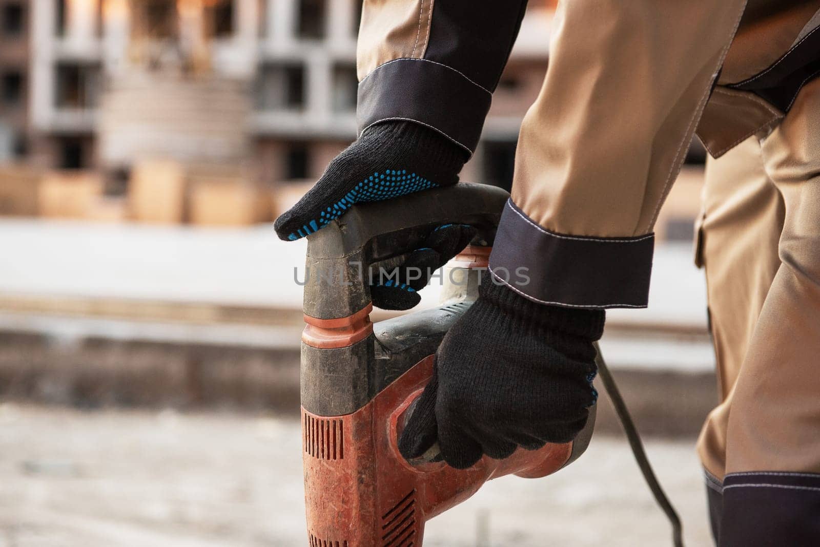 The builder with hammer drill perforator equipment at construction site background.