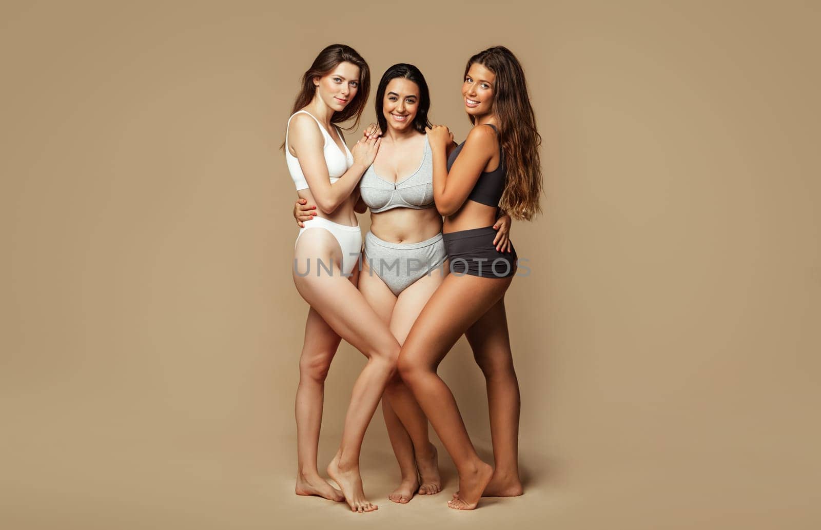Smiling young international women in different underwear, body types, enjoy natural beauty, isolated on beige background, studio, full length. Fashion, lifestyle, health care, support