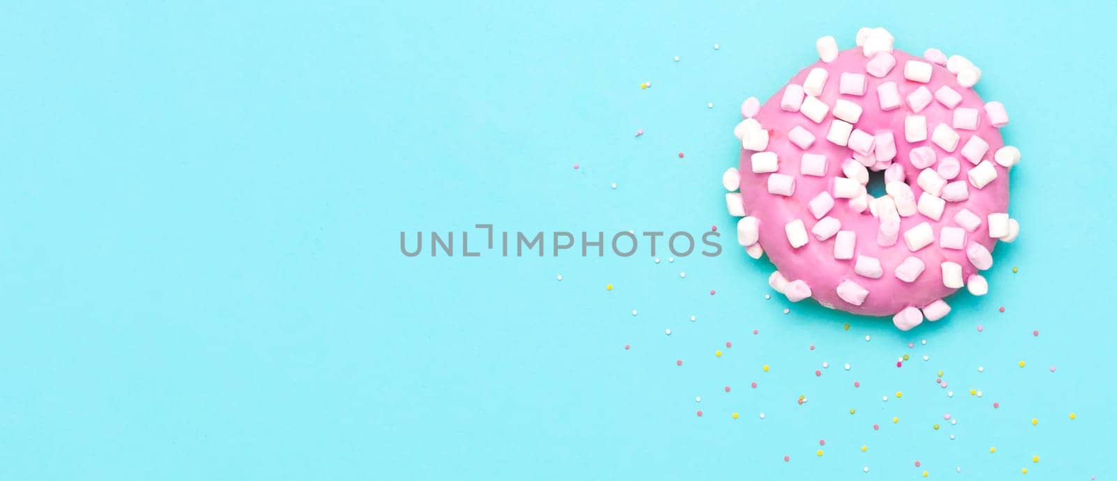 Pink donut with murshmallow and sprinkles, top view on blue background