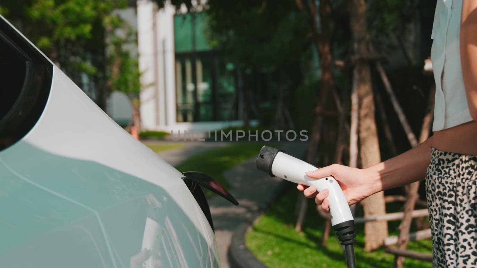 Young woman recharge EV electric car battery at residential area EV charging station in smart home with sustainable green renewable clean energy lifestyle for electric vehicle urban commute innards