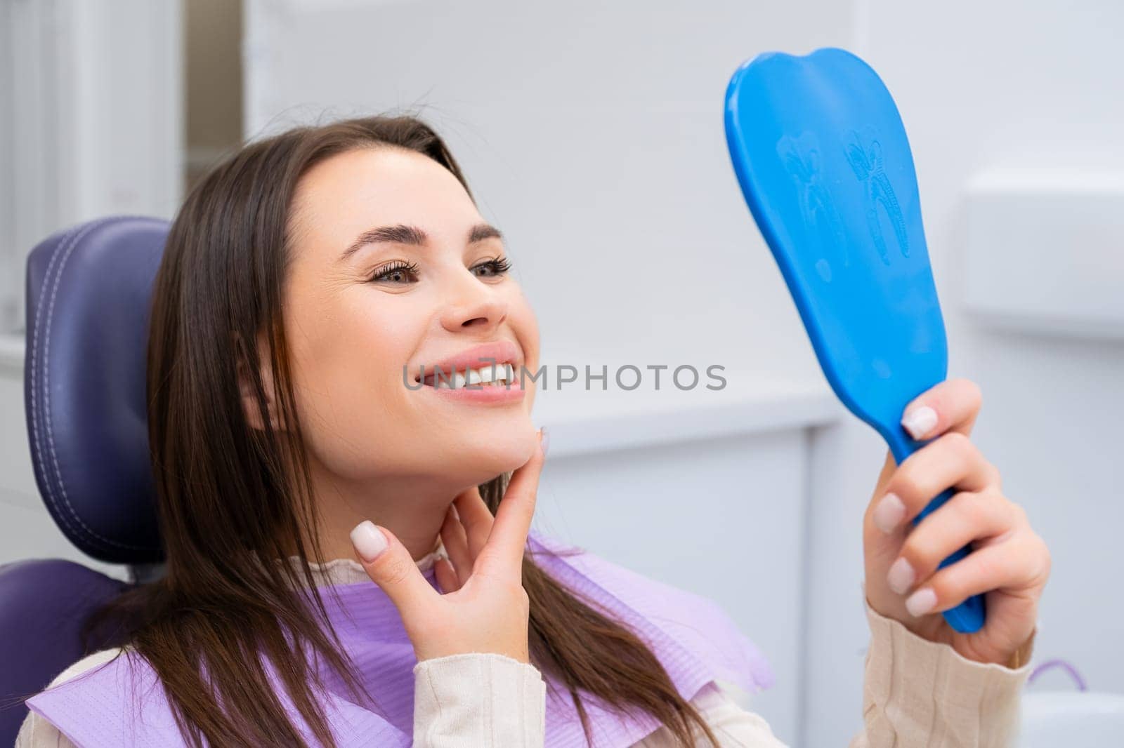 Female patient looks contentedly in the mirror while sitting in the dental chair by vladimka