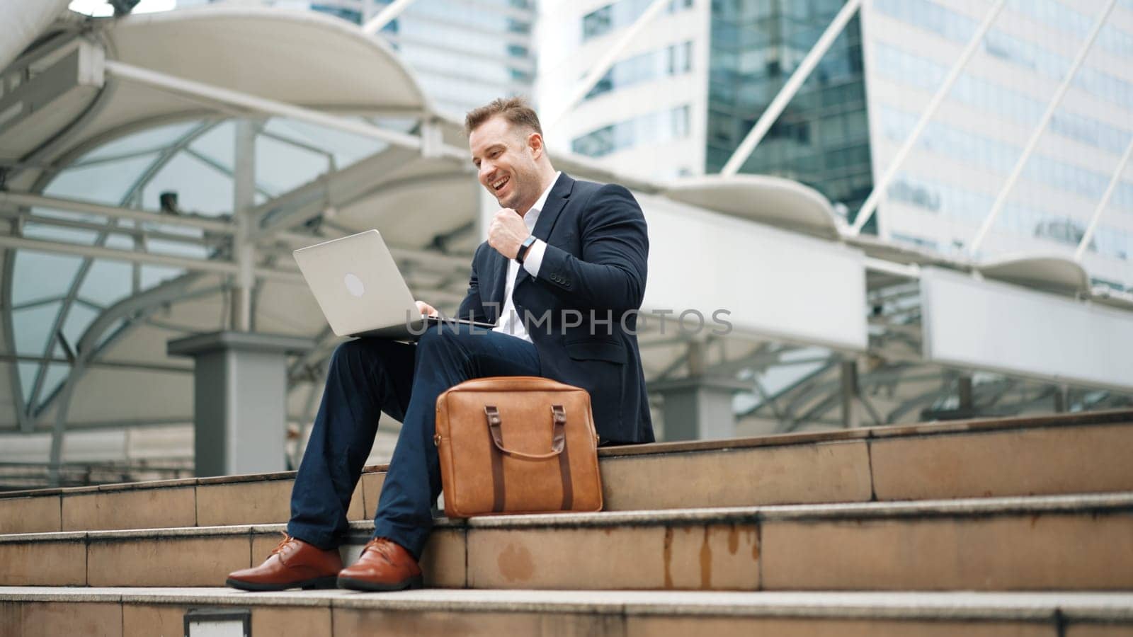 Close up of business man talking phone and celebrate successful project while sitting at stairs surrounded by urban city view. Smart caucasian manager happy while hear about increasing sales. Urbane.