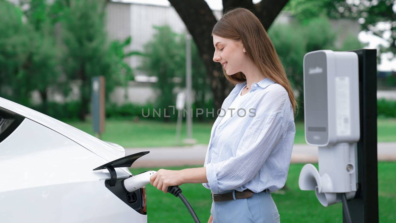 Woman recharging battery for electric car during road trip. Exalt by biancoblue