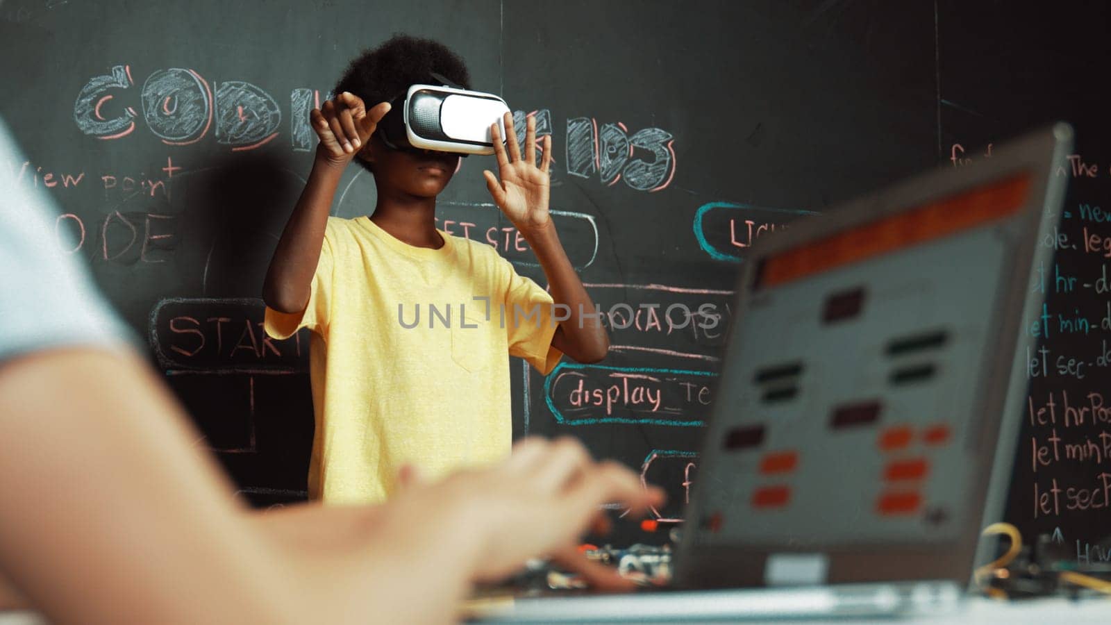 Closeup of school girl hand coding program while african student using VR interact with metaworld. Smart boy wearing virtual reality glasses and playing video games at innovative class. Edification.