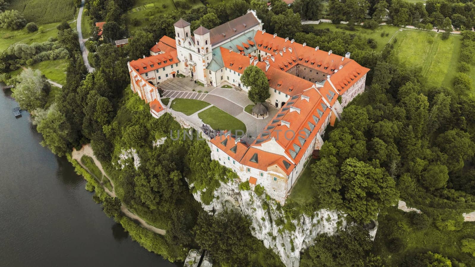 Aerial view of Benedictine abbey of Saints Peter and Paul in Tyniec, Poland. Panoramic view from drone of monastery courtyard, roofs and towers of stone buildings, green lawn of catholic church