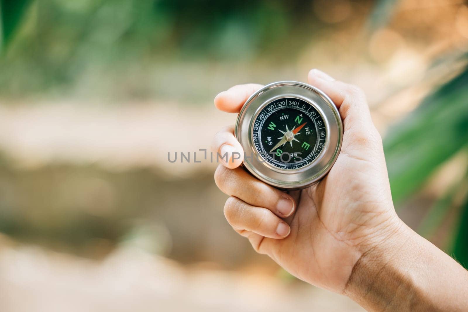 Hiker relies on compass to find direction in forest confusion. compass firmly held by traveler symbolizes leadership and exploration amidst nature helping her map position on journey of discovery. by Sorapop