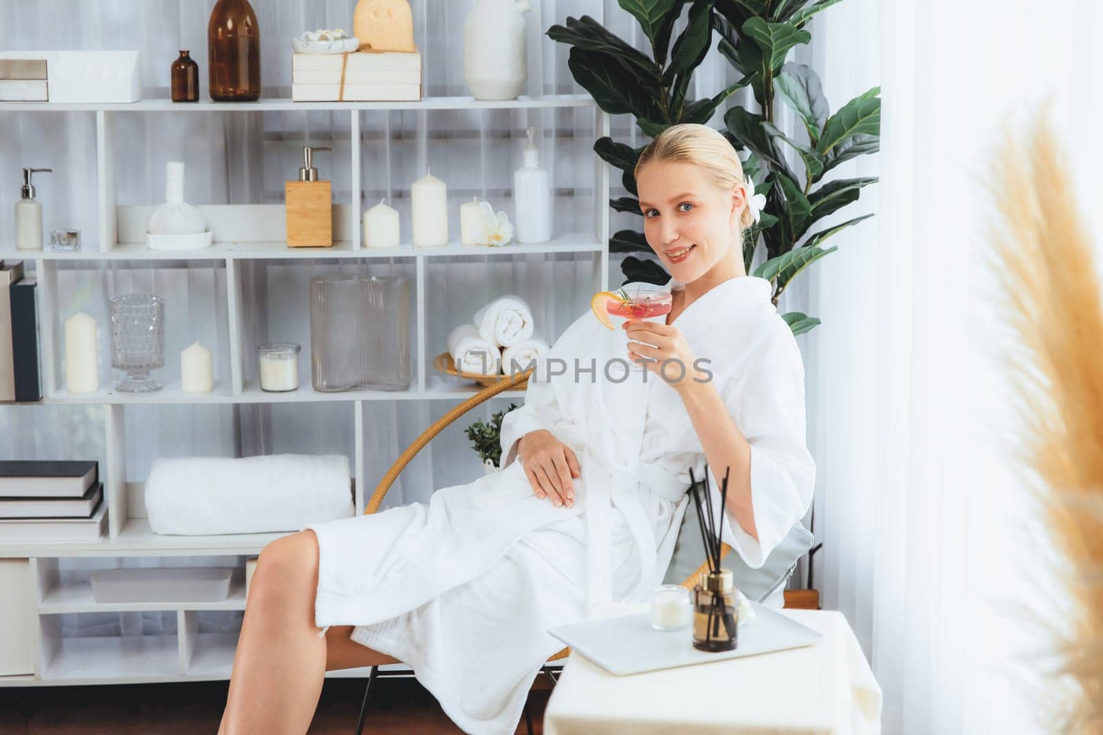 Beauty or body treatment spa salon vacation lifestyle concept with woman wearing bathrobe relaxing with drinks in luxurious hotel spa or resort room. Vacation and leisure relaxation. Quiescent