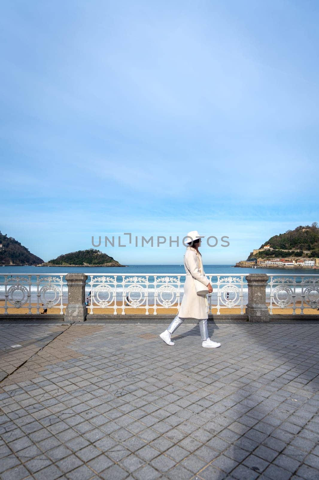 Stylish woman with white coat and hat on Paseo de la Concha, San Sebastian