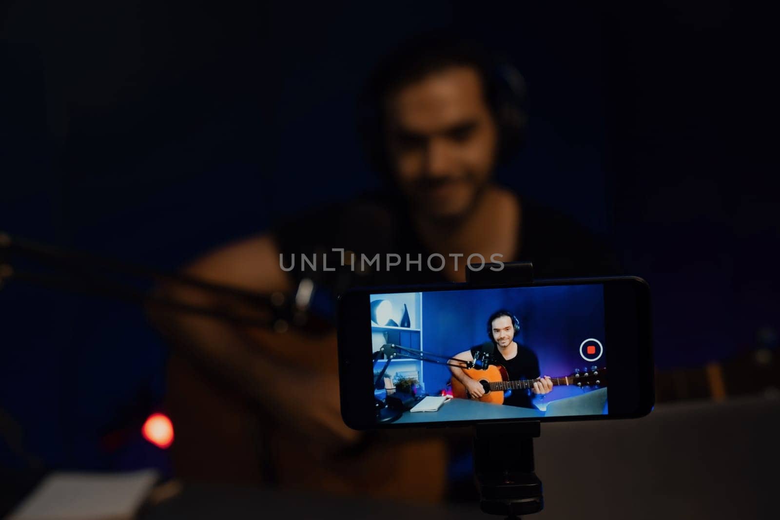 Host channel of smart influencer in creative audio with clearly smartphone live streaming with blur background, sing with play guitar music blogger social media online at neon light studio. Surmise.