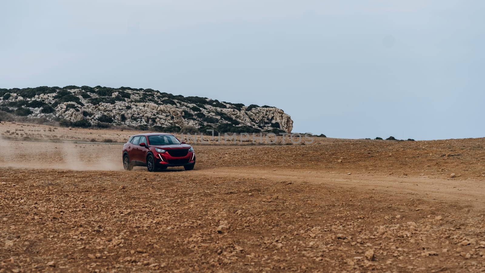 Red modern car driving on desert dirt road in cloud of dust, Cape Greco National Park in Cyprus