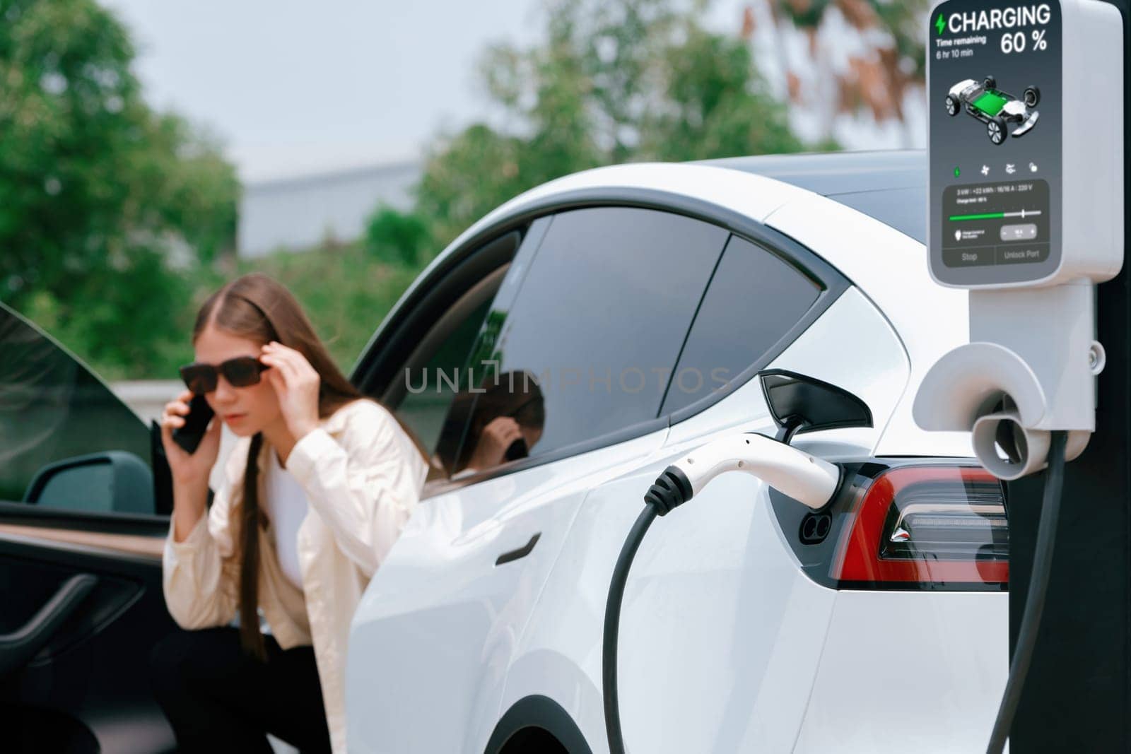 Young woman recharge her EV electric vehicle at green city park. Expedient by biancoblue