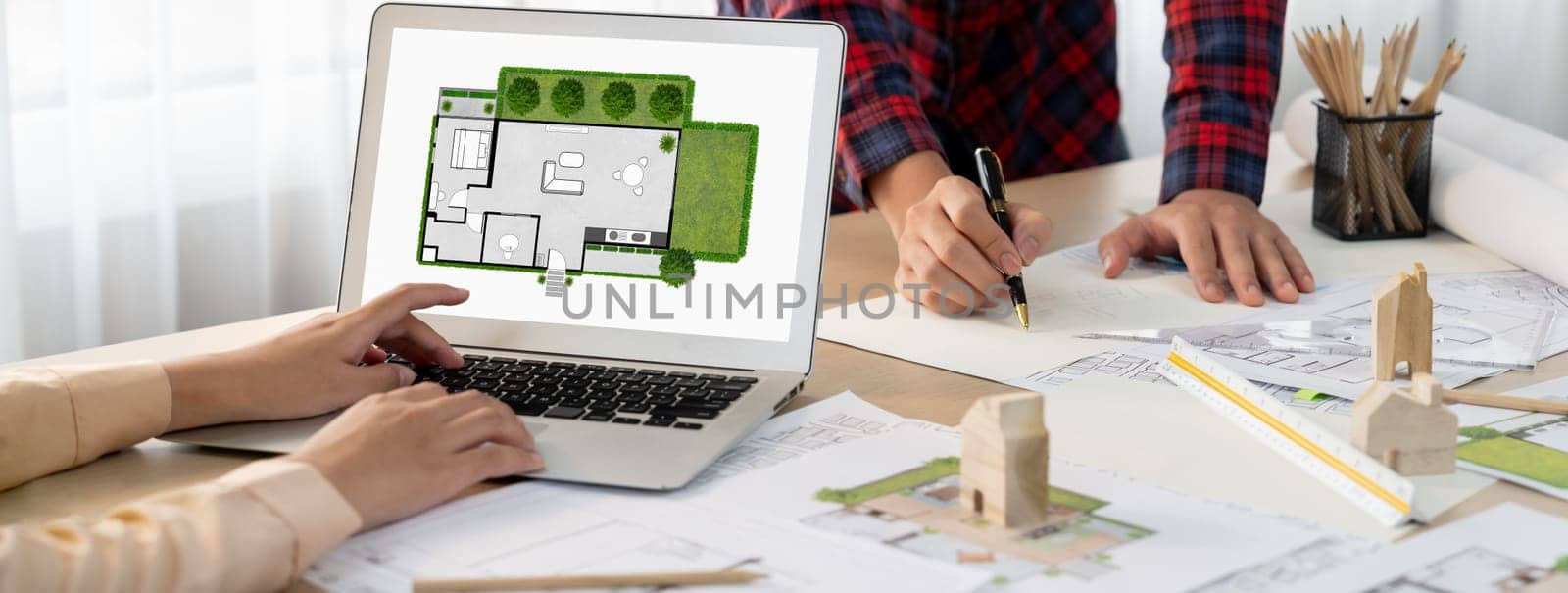 Professional architect represented ECO house displayed on laptop to project manager on messy table with wooden block, blueprint, architectural document placed at modern office. Close up. Delineation.
