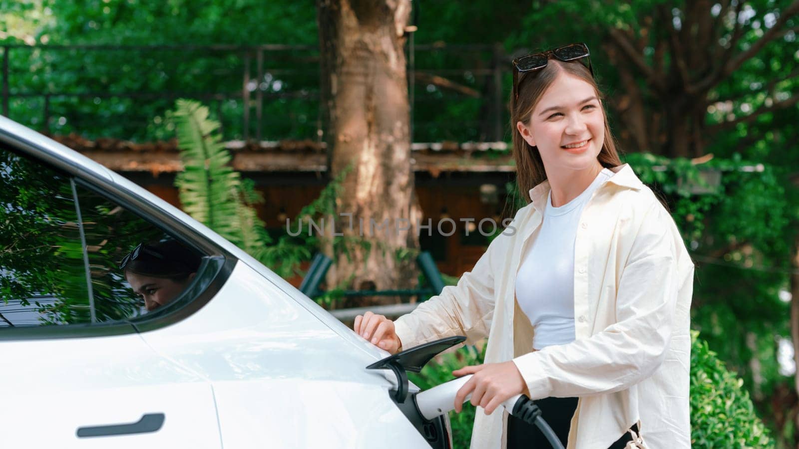 Young woman recharge her EV electric vehicle at green city park. Expedient by biancoblue