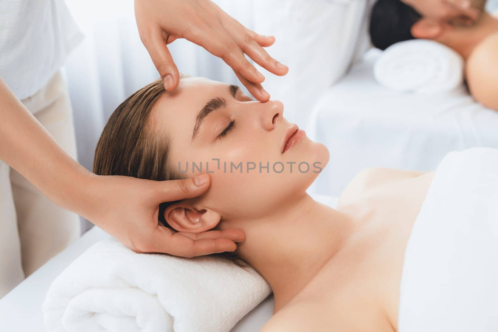 Caucasian couple enjoying relaxing anti-stress head massage and pampering facial beauty skin recreation leisure in dayspa modern light ambient at luxury resort or hotel spa salon. Quiescent