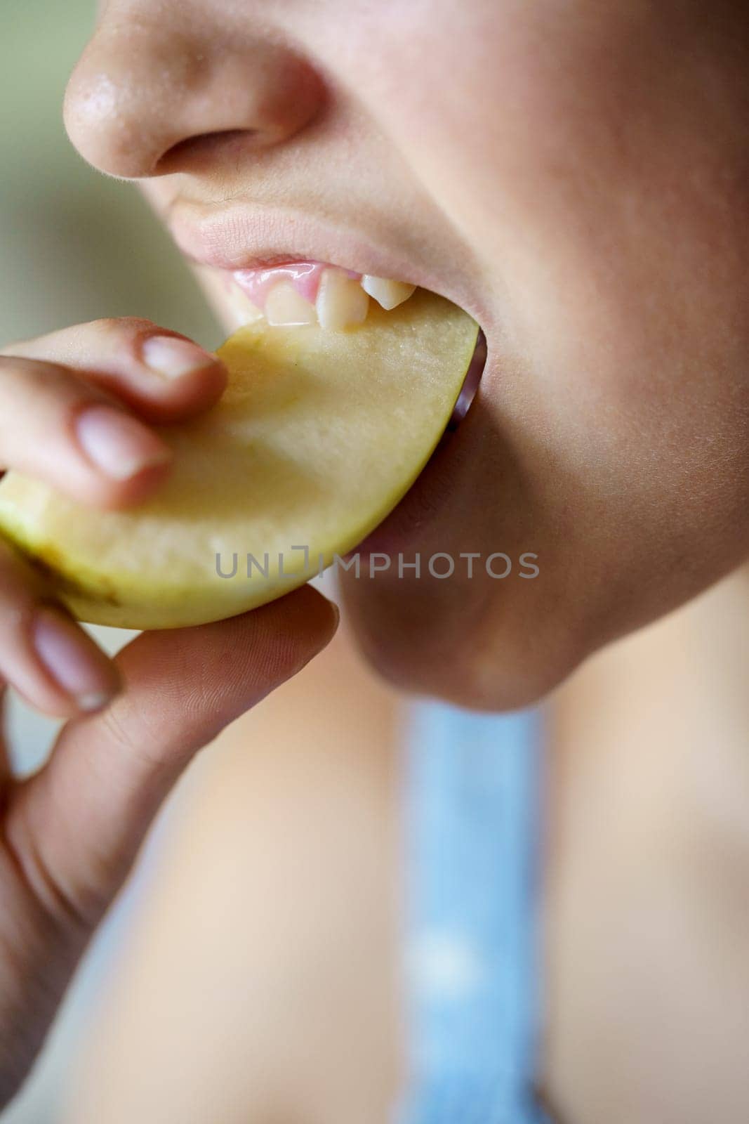 Closeup of crop anonymous teenage girl biting fresh juicy apple slice at home