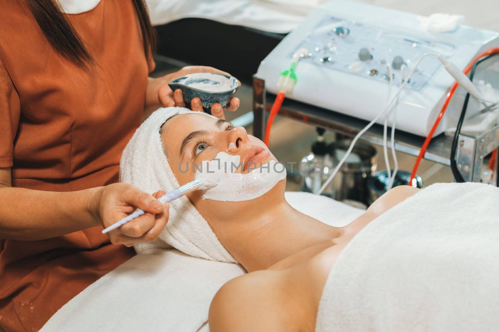 Beautiful young women lie on spa bed while having facial massage from professional doctor. Attractive female with beautiful skin surrounded by electric facial machine. Tranquility.