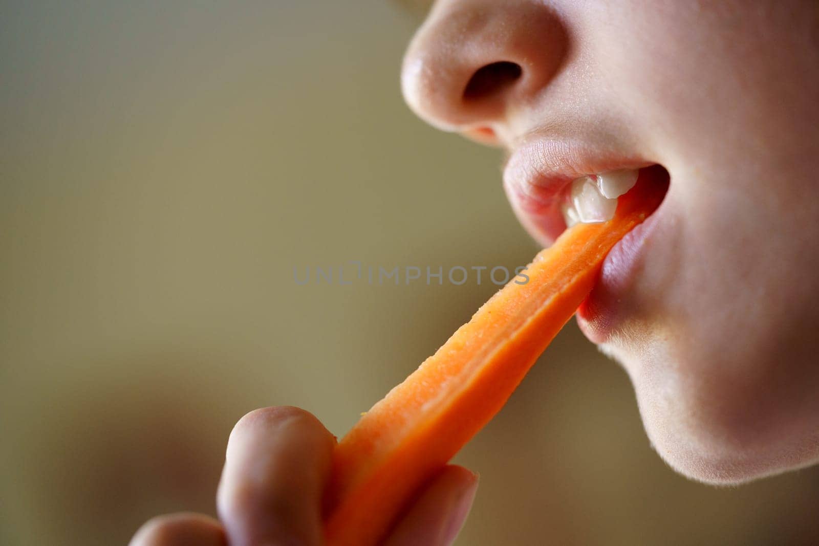 From below of crop anonymous teenage girl eating fresh organic carrot slice at home